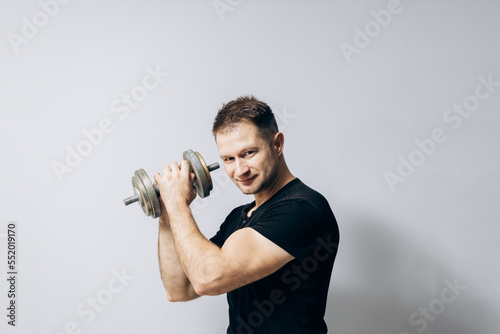 Sports guy does morning exercises with dumbbells. Muscular man holds a dumbbell in one hand. Sports, health.