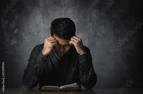 Asian man reading book or bible hand over head having stressful depression sad time sitting on the table. Depression man sad serios reading book. Education learning bible religion concept.