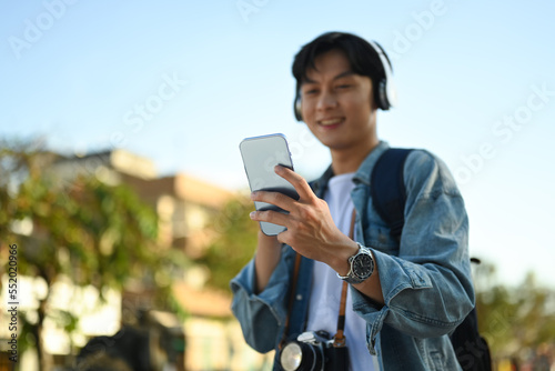 Smiling asian man traveler in headphone using smartphone platform applications for helping tourism about travel map GPS