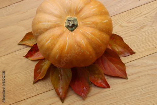 Fresh pale orange pumpkin with autumnal  leaves on wooden backgroud photo