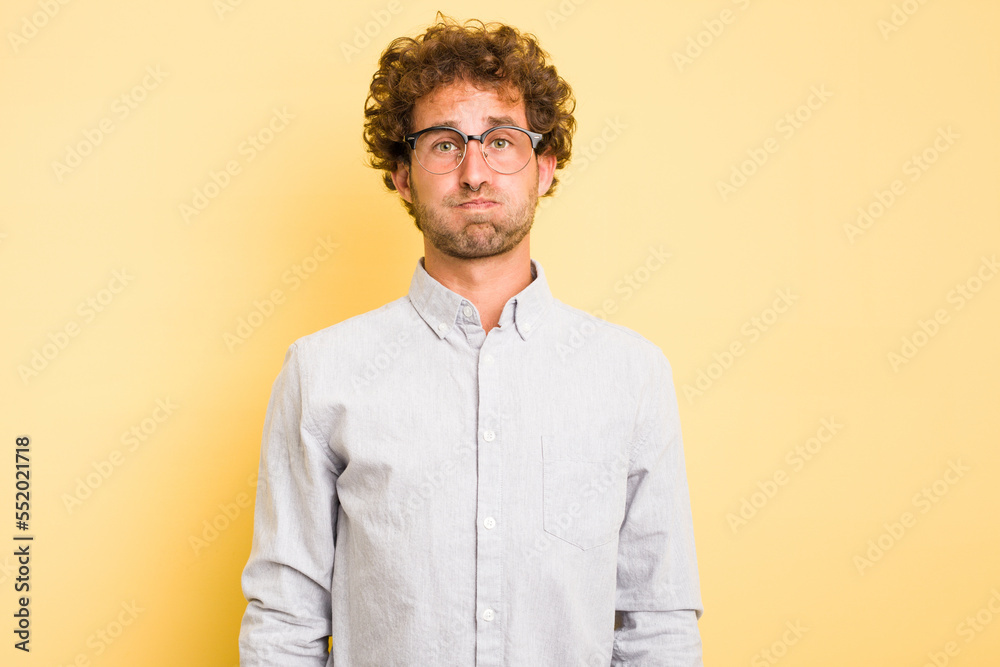 Young smart caucasian man on yellow background blows cheeks, has tired expression. Facial expression concept. Young smart caucasian man on yellow background blows cheeks, has tired expression. Facial expression concept.
