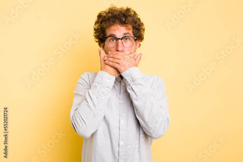 Young smart caucasian man on yellow background covering mouth with hands looking worried.