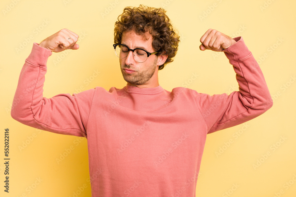 Young smart caucasian man on yellow background showing strength gesture with arms, symbol of feminine power Young smart caucasian man on yellow background showing strength gesture with arms, symbol of feminine power