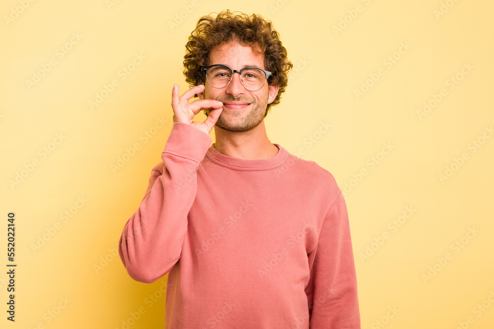 Young smart caucasian man on yellow background with fingers on lips keeping a secret.