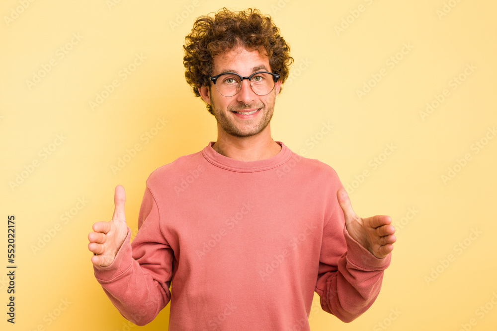 Young smart caucasian man on yellow background holding something with both hands, product presentation. Young smart caucasian man on yellow background holding something with both hands, product presentation.