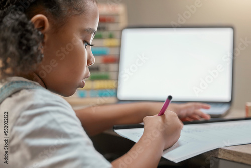Home, elearning and little girl writing on paper with mockup screen on laptop for education. Focus, remote student and black child busy with homework at study desk in house with concentration.