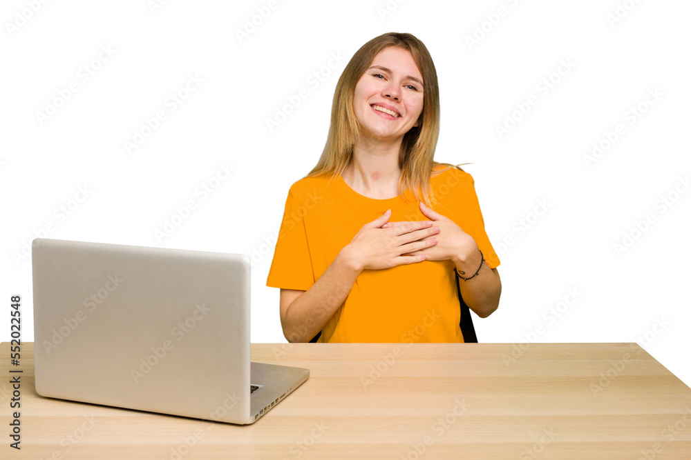 Young caucasian woman in a workplace working with a laptop isolated has friendly expression, pressing palm to chest. Love concept. Young caucasian woman in a workplace working with a laptop isolated has friendly expression, pressing palm to chest. Love concept.