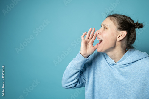 Profile of a European alarmed woman who screams loudly, holding her hand to her mouth. Copy space. 