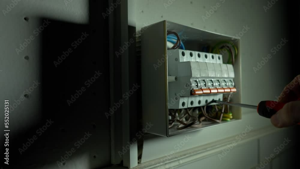 Electrician assembles electrical panel in dark. Close up of a mans hands tightening a screw with a screwdriver. Turning on high voltage electrical switches in a switchboard and light turned on. Electrician assembles electrical panel in dark. Close up of a mans hands tightening a screw with a screwdriver. Turning on high voltage electrical switches in a switchboard and light turned on.