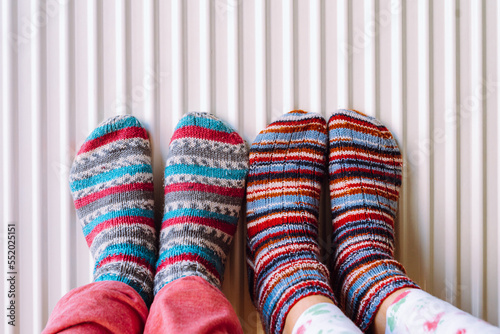 Two pairs of legs in knitted socks made of multi-colored woolen threads on heating radiator