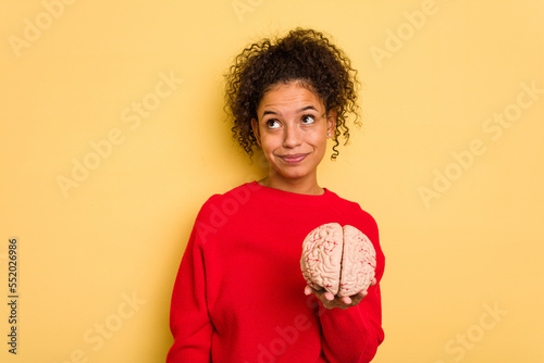Young brazilian woman holding a brain model isolated dreaming of achieving goals and purposes