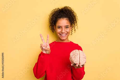 Young brazilian woman holding a brain model isolated showing number two with fingers.