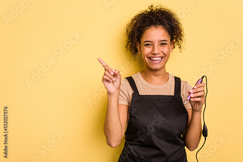 Young African american manicurist woman holding an electric file drill isolated smiling and pointing aside, showing something at blank space.