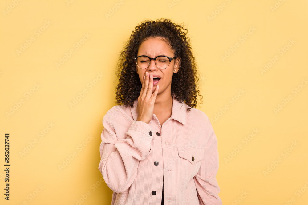 Young Brazilian curly hair cute woman isolated on yellow background yawning showing a tired gesture covering mouth with hand. Young Brazilian curly hair cute woman isolated on yellow background yawning showing a tired gesture covering mouth with hand.