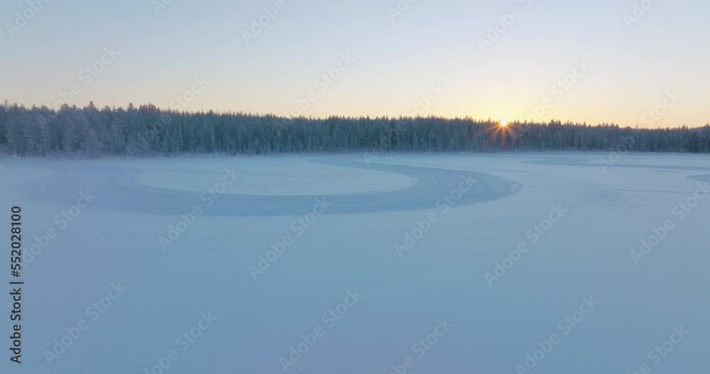 Curving tyre tracks on Norbotten Polar circle woodland ice lake aerial view rising to glowing sunrise skyline Curving tyre tracks on Norbotten Polar circle woodland ice lake aerial view rising to glowing sunrise skyline
