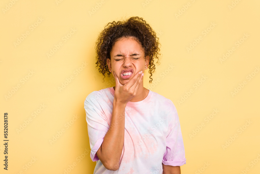 Young Brazilian curly hair cute woman isolated on yellow background having a strong teeth pain, molar ache. Young Brazilian curly hair cute woman isolated on yellow background having a strong teeth pain, molar ache.