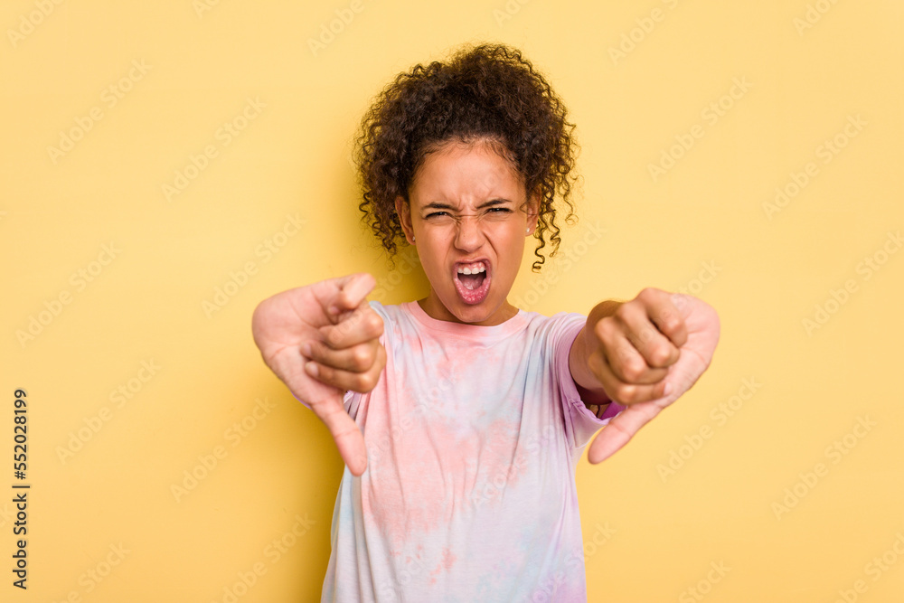 Young Brazilian curly hair cute woman isolated on yellow background showing thumb down and expressing dislike. Young Brazilian curly hair cute woman isolated on yellow background showing thumb down and expressing dislike.