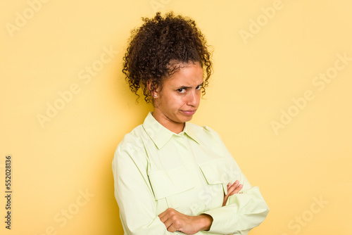 Young Brazilian curly hair cute woman isolated on yellow background suspicious, uncertain, examining you. © Asier