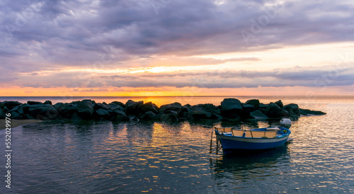 boat in morning or evening sea with rock pier and amazing sunrise or sunset with nice clouds on background of landscape