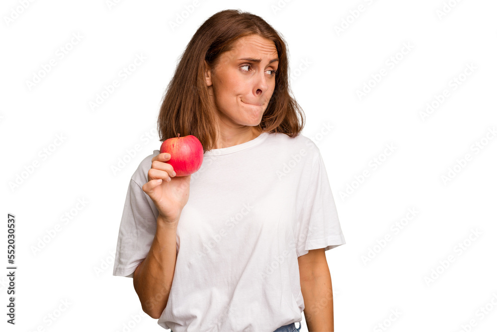 Young caucasian woman holding a red apple isolated confused, feels doubtful and unsure. Young caucasian woman holding a red apple isolated confused, feels doubtful and unsure.