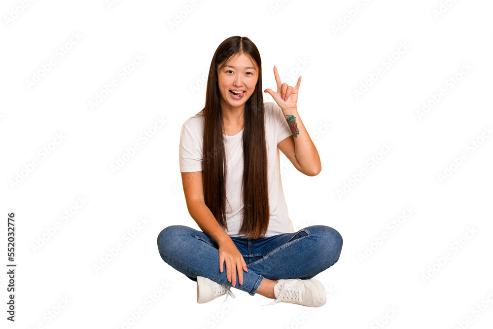 Young asian woman sitting on the floor cutout isolated showing a horns gesture as a revolution concept. Young asian woman sitting on the floor cutout isolated showing a horns gesture as a revolution concept.