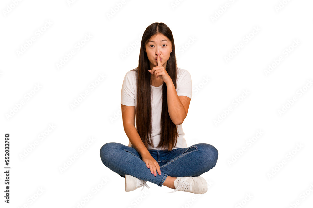 Young asian woman sitting on the floor cutout isolated keeping a secret or asking for silence.