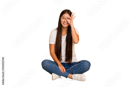 Young asian woman sitting on the floor cutout isolated excited keeping ok gesture on eye.