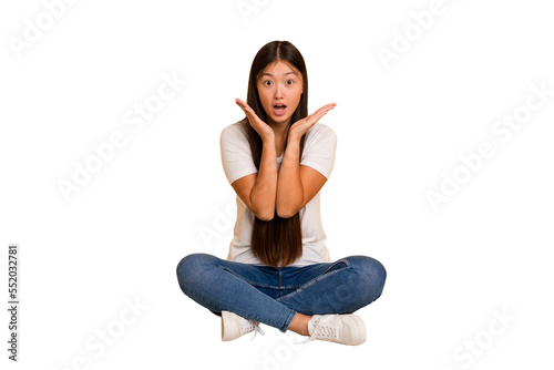 Young asian woman sitting on the floor cutout isolated surprised and shocked.