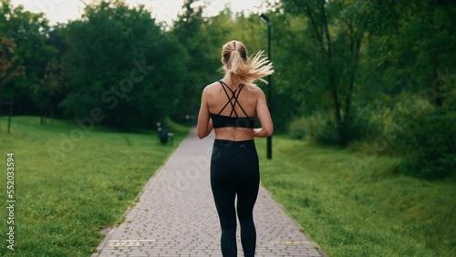 Back view of the female athlete is running in the park wearing black sportswear. Following shot active female runner. Sport people concept.