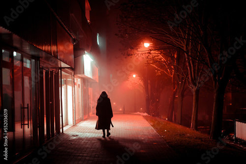 a lonely woman in a coat walks through a foggy city at night