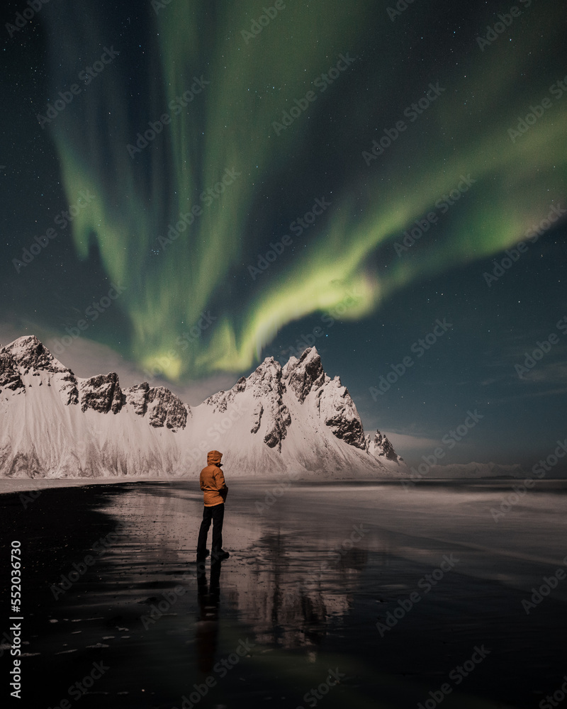 Northern lights, aurora borealis over Vestrahorn mountains in Iceland and with person who is looking up on sky during winter. 