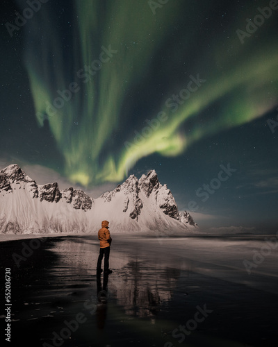 Northern lights  aurora borealis over Vestrahorn mountains in Iceland and with person who is looking up on sky during winter. 