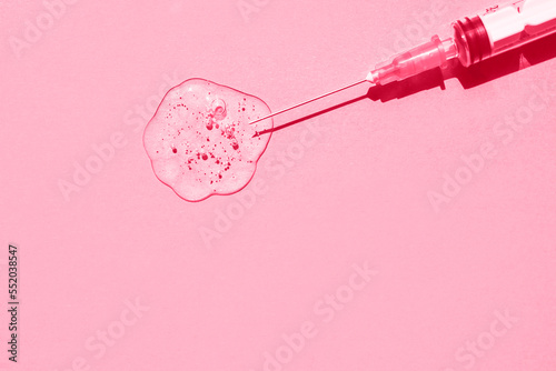 Sterile medical syringe and drop of gelatinous liquid on pink background. Demonstration of colors 2023 Viva Magenta. Flat plan, space for text. photo
