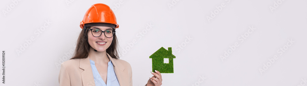 A girl in a construction helmet holds a green house. The concept of ecological clean housing. A girl in a construction helmet holds a green house. The concept of ecological clean housing.
