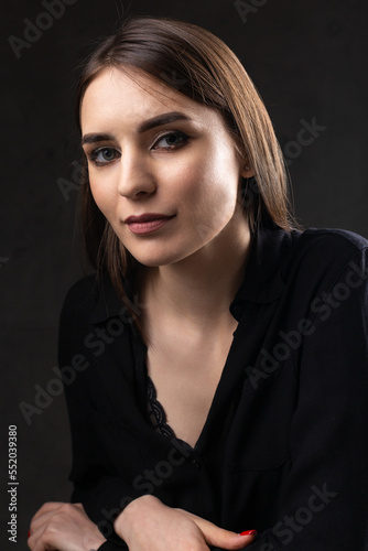 Portrait of a young brunette with long hair in the studio. Dramatic photo in dark colors.