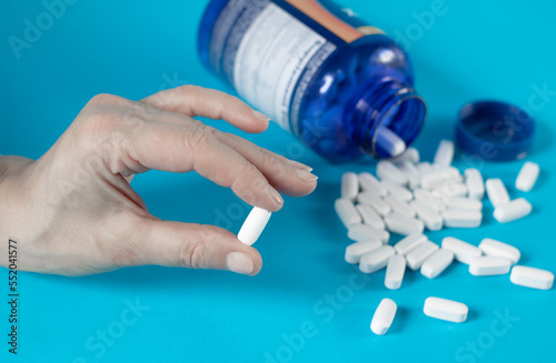 Female fingers hold a large white pill with bioadditives on a blue background photo