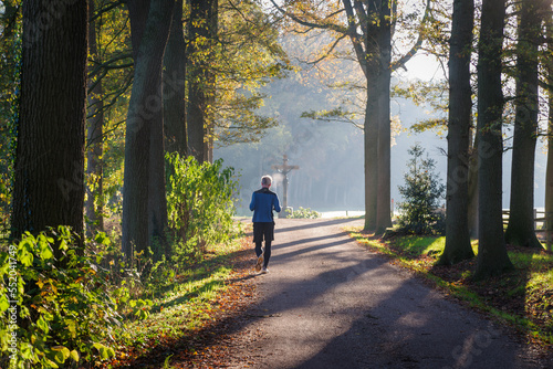 OLDENZAAL, NETHERLANDS - NOVEMBER 20, 2022: Senior jogger running on a sunny autumn day in a beautiful natural surroundings.