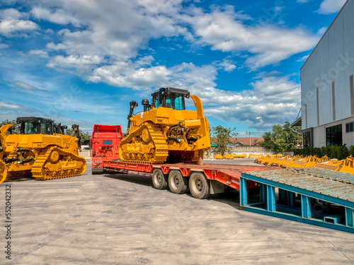 Heavy new yellow excavator on transportation truck with long trailer platform.