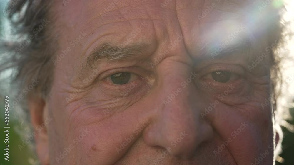 One mature senior man close up face and eyes with sunlight flare outside. Macro close up of older male person with wrinkled eyes looking at camera One mature senior man close up face and eyes with sunlight flare outside. Macro close up of older male person with wrinkled eyes looking at camera