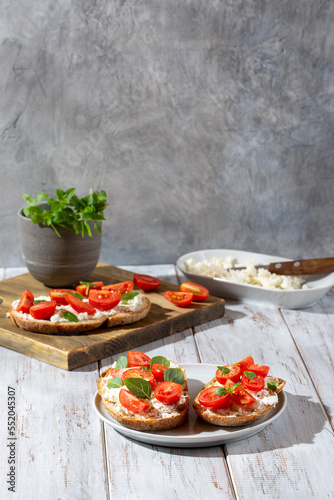 Sandwich with cottage cheese, tomatoes and basil on white wooden background. Traditional Italian bruschetta. Healthy savory feta and tomato toast. Copy space.