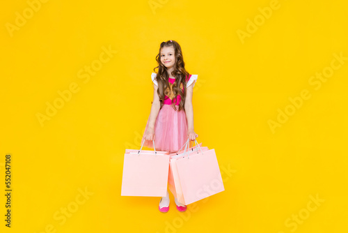 A girl in a pink dress is holding large bags of new things in her hands. New purchases for the summer, shopping at the mall.