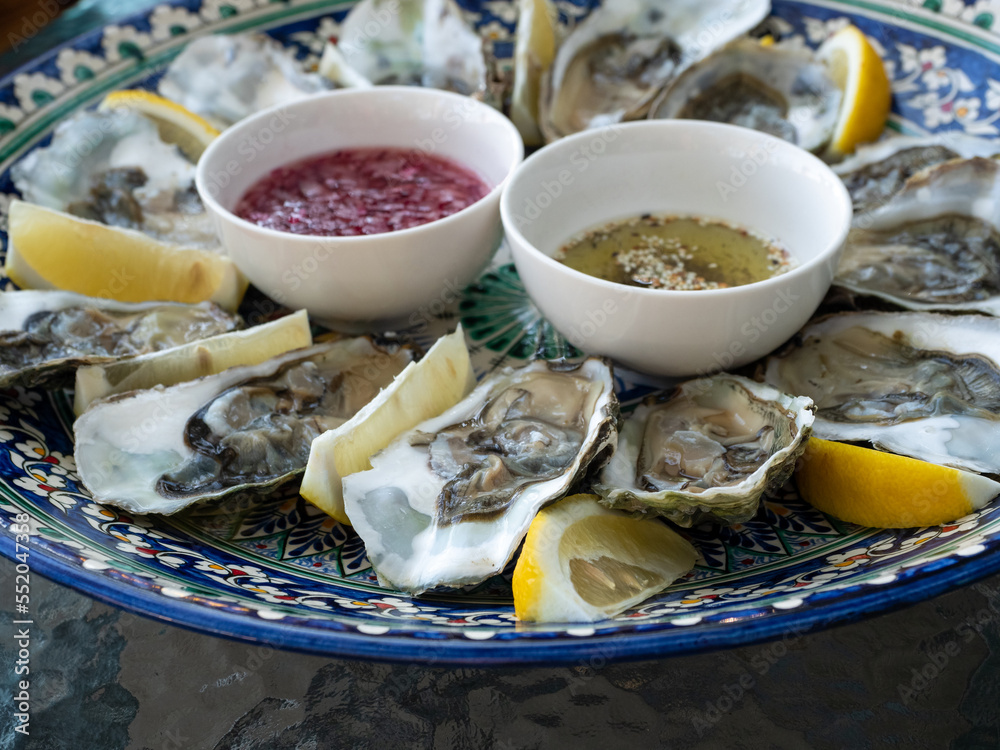 Fresh opened oysters served with different sauces and lemon wedges on plate. Close-up.