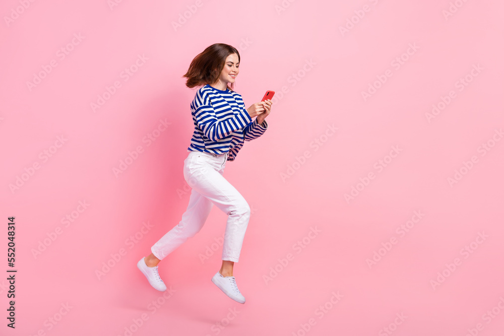 Full size portrait of cheerful sporty girl jump hurry run use telephone isolated on pink color background