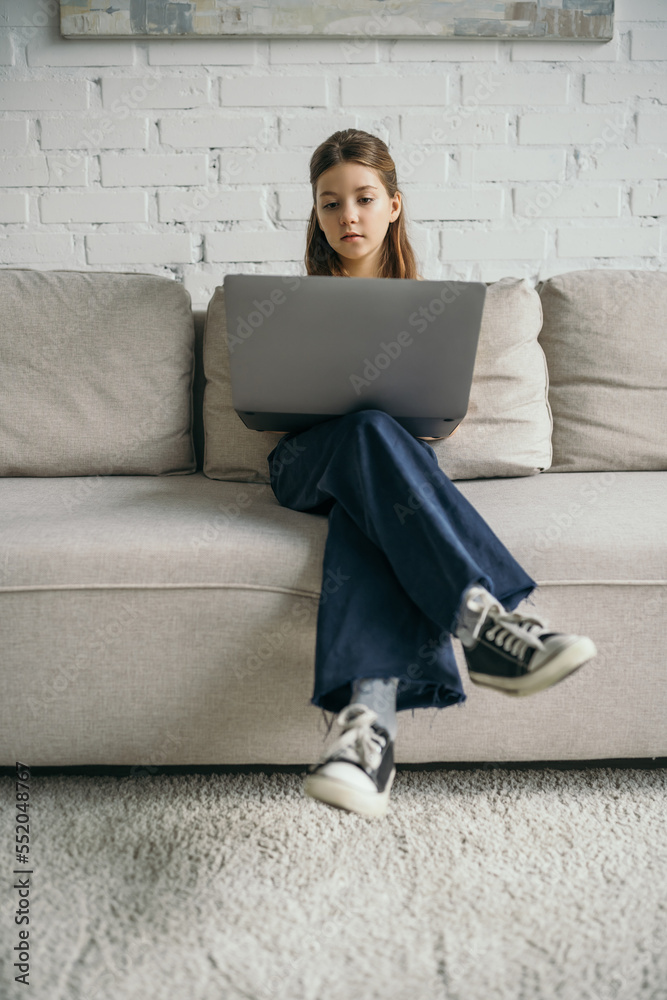 preteen girl with laptop sitting on modern comfortable couch at home