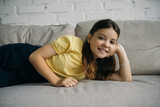 brunette girl smiling at camera while resting on couch in living room