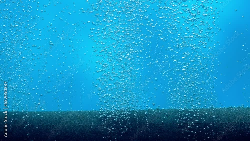 Lot of small shiny air bubbles escaping from compressor tube or filter under water on blue background. Close up of working equipment for aeration of water with oxygen in aquarium. Slow motion.