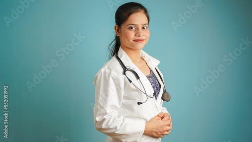 Portrait of a young female doctor wearing apron and stethoscope  Cheerful Asian Indian woman doctor isolated over blue studio background