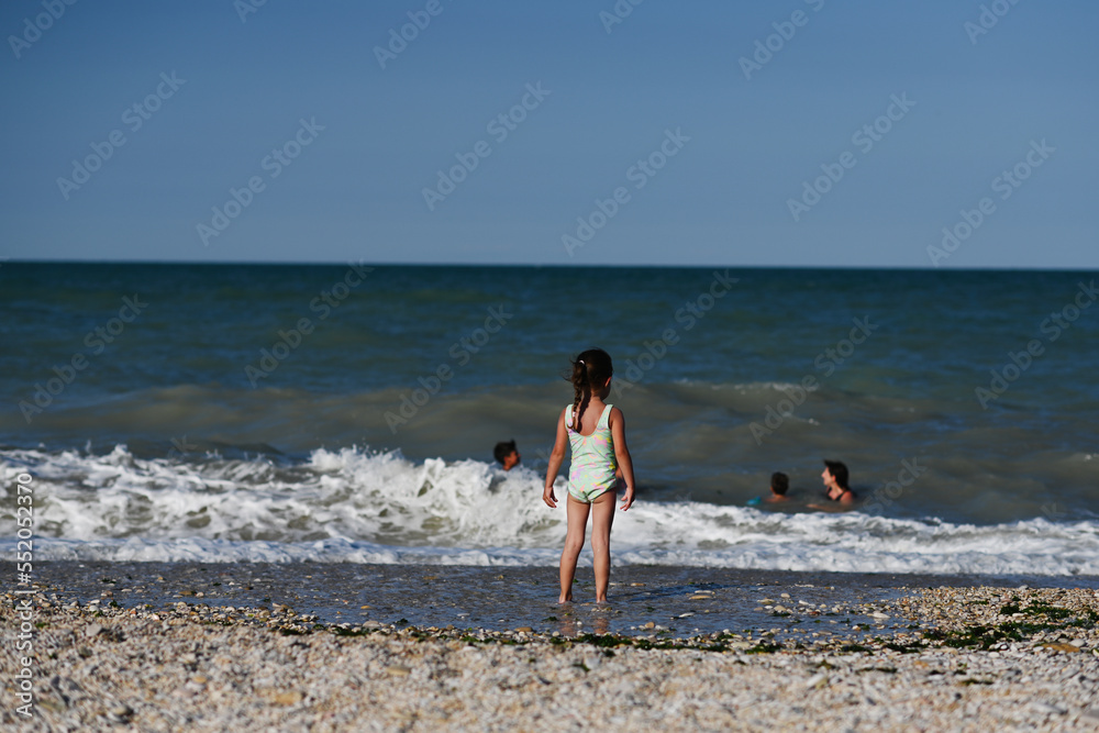 Back of baby girl looking on her family swimming at sea in beach Porto Sant Elpidio, Italy.