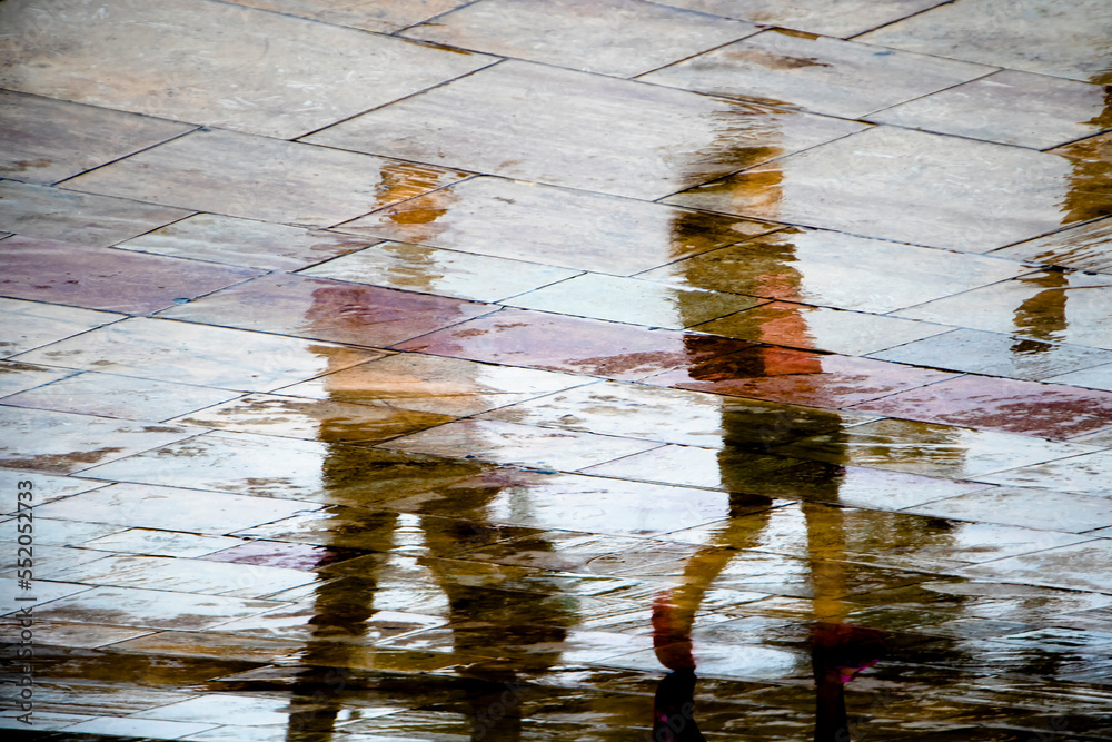 Fototapeta Abstract blurry silhouette reflections of unrecognizable people walking on wet c