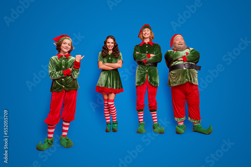 Full size photo of happy cheerful santa helper hands crossed wear hat point finger isolated on red color background